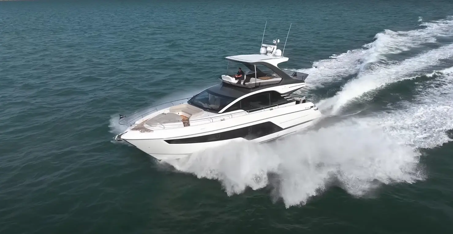 A luxury motor yacht speeds across turquoise waters, creating white spray; a person steers from the flybridge.